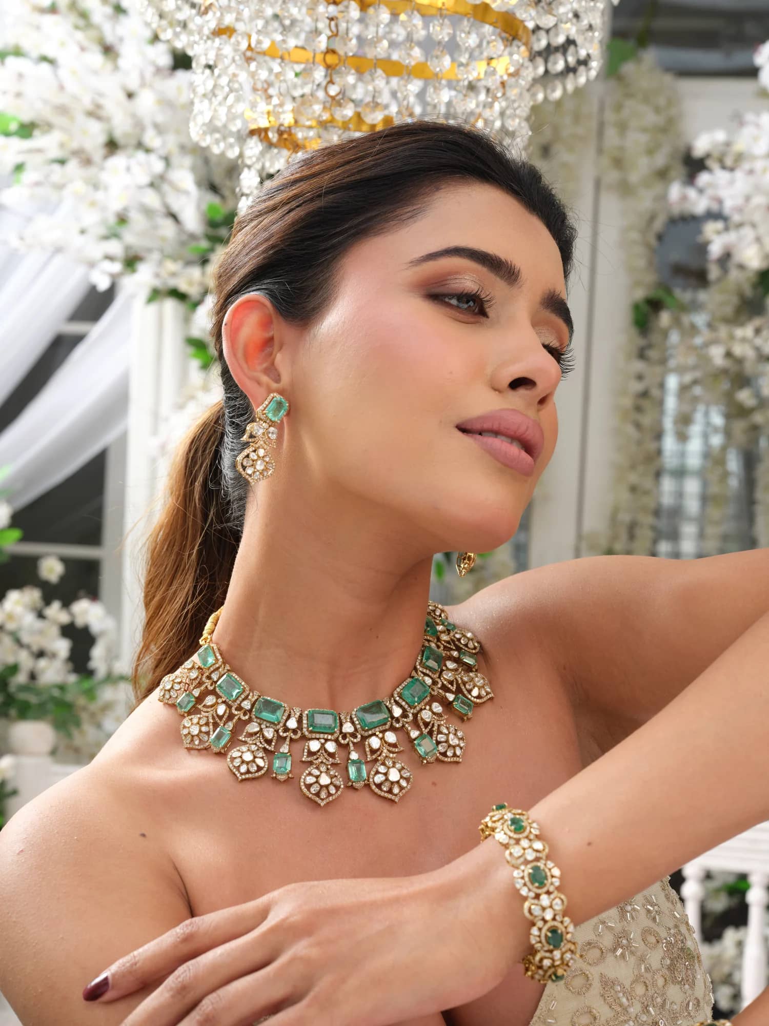 A model wearing the Inara open-polki choker with emerald-cut stones, matching drops and bracelet, in the blossom pavilion